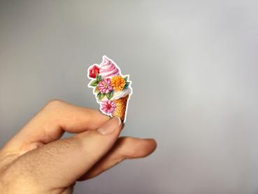 Hand, die einen Aufkleber in Form einer Eistüte mit Blumenmotiven hält, gestaltet von DreamArt VM.